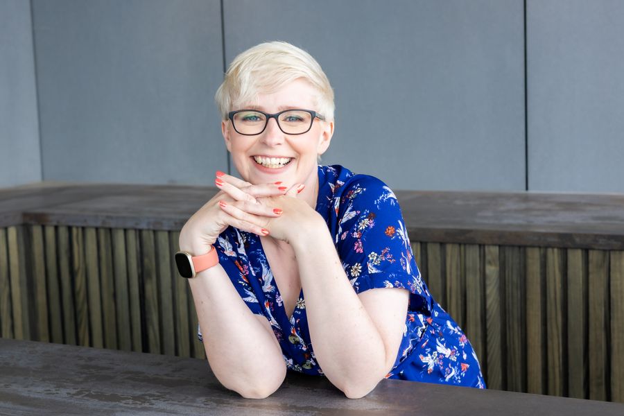 Jenny Lucas in a blue patterned dress, chin resting on her hands, smiling broadly
